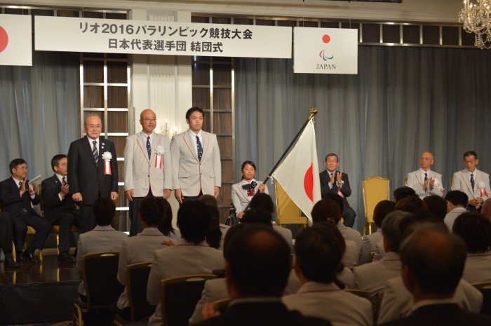 団旗が鳥原光憲JPC（日本パラリンピック委員会）会長から、団長・大槻洋也、主将で車いすバスケットボールの藤本怜央（SUS）、騎手で車いすテニスの上地結衣（エイベックス）へと授与された