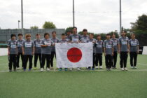 応援メッセージが書かれた日本国旗を掲げての選手・スタッフ集合写真 　筆者撮影